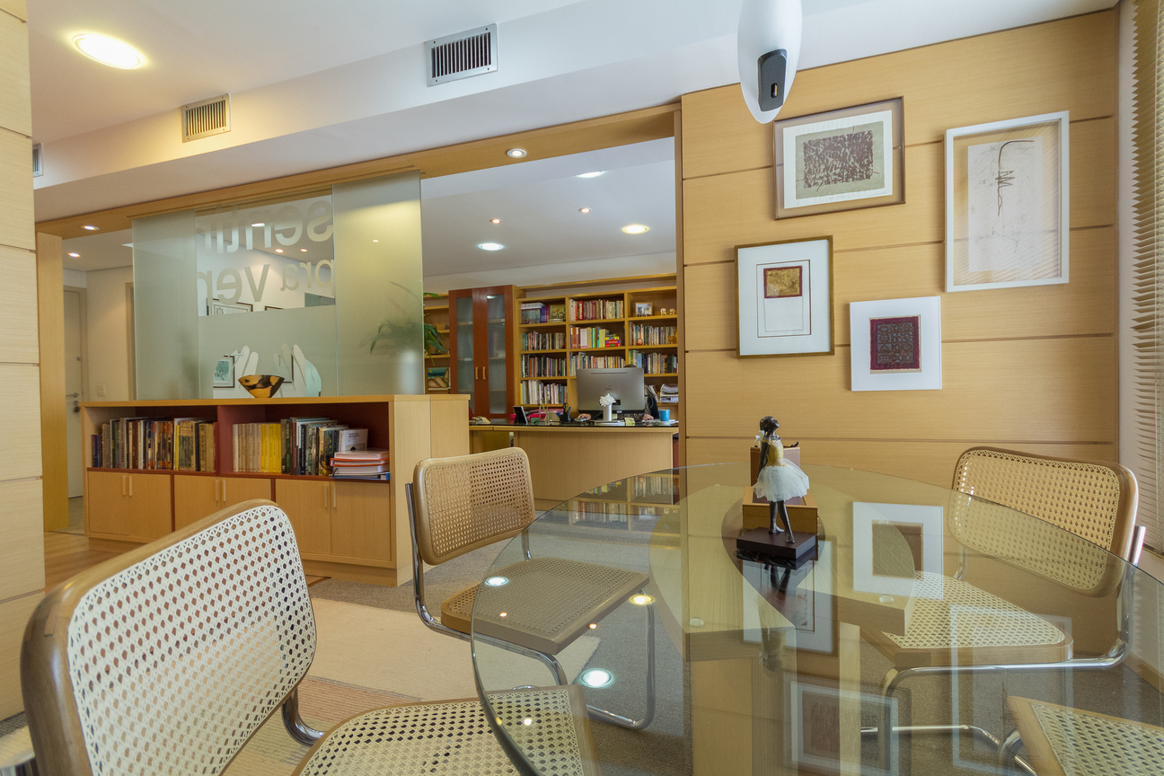 Foto do escritorio Arteinclusão com mesas de vidro cadeiras, quadros e estante com diversos livros foto do escritório da Arteinclusão